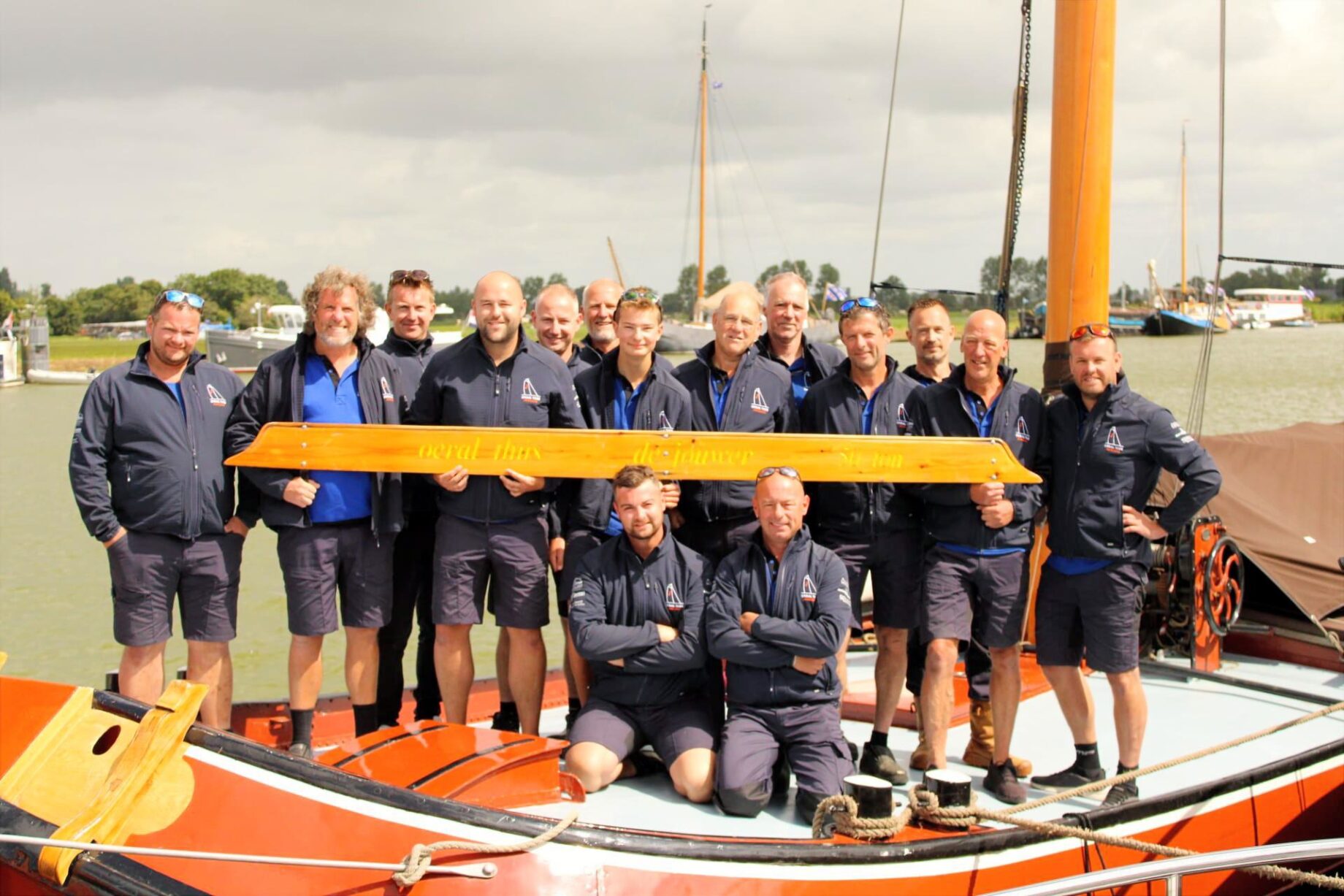 De voltallige bemanning van Oeral Thús aan dek, achter het naambord van het schip